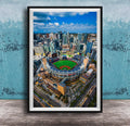 An aerial view of a baseball stadium surrounded by a city skyline, with tall buildings and a clear blue sky in the background.