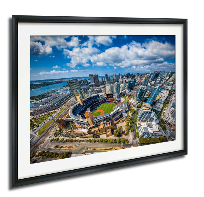 The image is an aerial view of a large city with a baseball stadium in the center, surrounded by tall buildings and a body of water in the background.