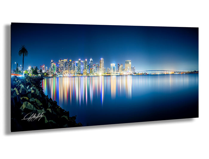 A stunning nighttime cityscape with a skyline of illuminated buildings reflected in the calm waters of a large body of water, creating a mesmerizing and vibrant scene.