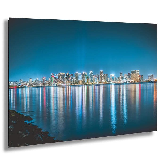 A stunning nighttime cityscape with a skyline of illuminated buildings reflected in the calm waters of a large body of water, creating a mesmerizing and vibrant scene.