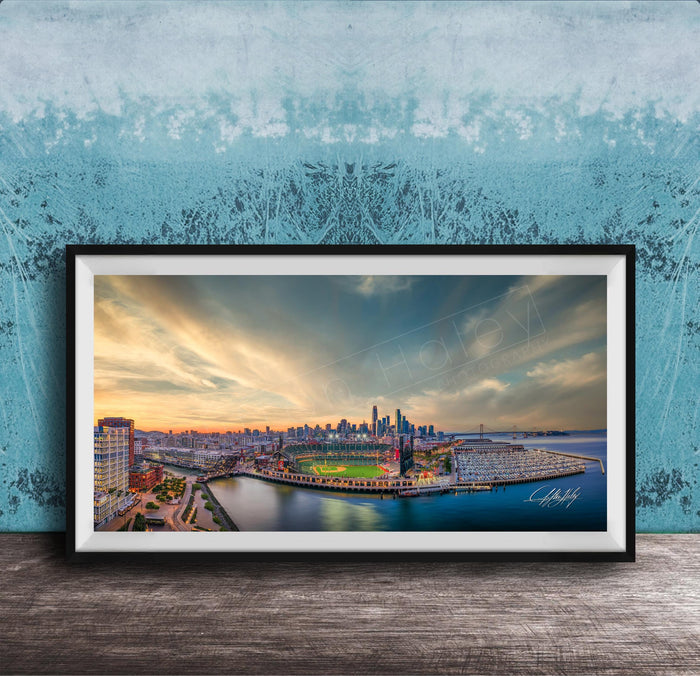 The image is a framed photograph of a cityscape at sunset, featuring a skyline with tall buildings and a body of water in the foreground.