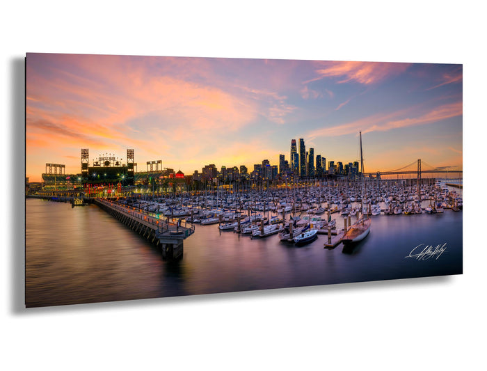 A panoramic view of a city skyline at sunset, with a marina filled with boats in the foreground.