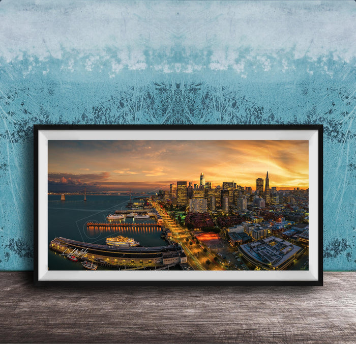 The image is a framed photograph of a cityscape at sunset, featuring a skyline with tall buildings and a harbor with boats.