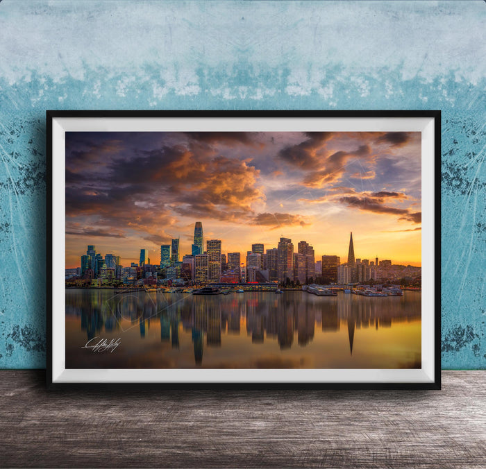 A framed photograph depicting a city skyline at sunset, with the city's buildings reflected in the water below.