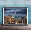 A framed photograph of a city skyline at night, with numerous illuminated skyscrapers and buildings against a dark sky.
