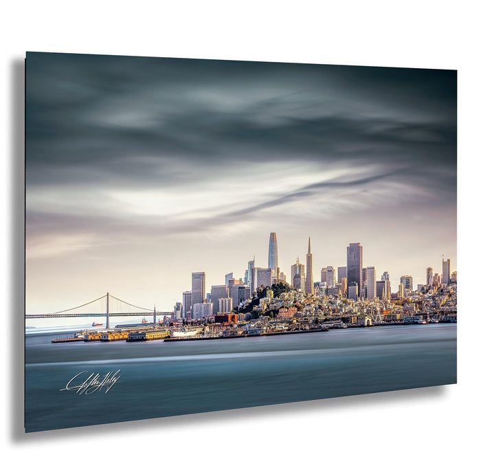 A panoramic view of the San Francisco skyline, with the Golden Gate Bridge and the city's iconic skyscrapers in the background. The sky is filled with clouds, creating a dramatic atmosphere over the cityscape.