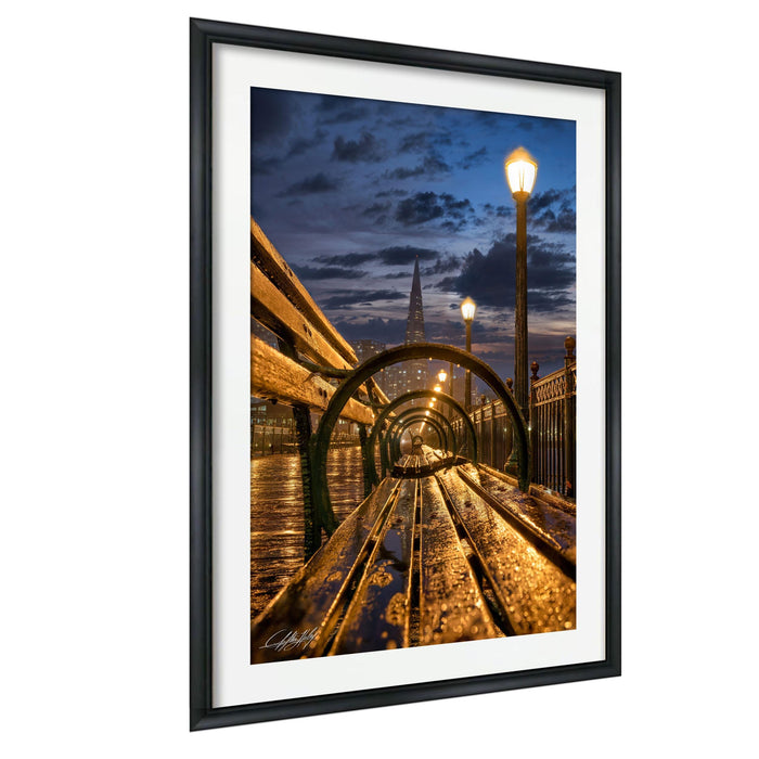 a wooden bench situated on a bridge, with a curved metal railing and a lamppost in the background, all illuminated by the warm glow of the setting sun.
