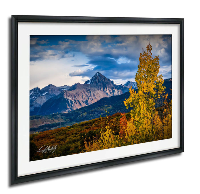 a breathtaking mountain landscape with a vibrant display of autumn foliage in the foreground, set against a stunning backdrop of snow-capped peaks and a dramatic cloudy sky.