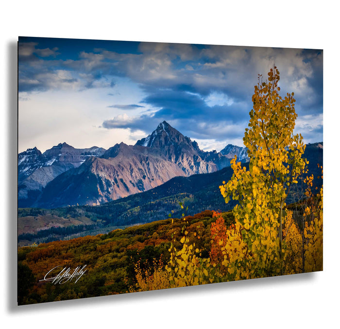 a breathtaking mountain landscape with snow-capped peaks, a vibrant mix of autumn foliage, and a dramatic cloudy sky.