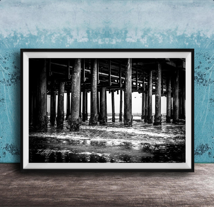 A black and white photograph of a pier with multiple columns and pillars, set against a blue textured wall.