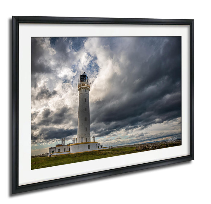 A white lighthouse with a black top stands tall against a dramatic sky filled with dark clouds.