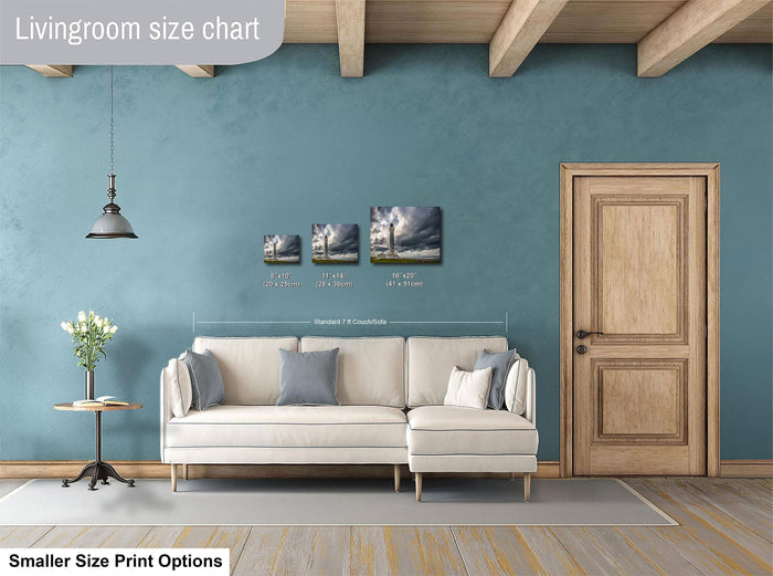 a living room with a white sofa, a wooden door, and a potted plant. There are three framed artworks hanging on the wall, each depicting a different landscape scene. The living room appears to be designed for relaxation and comfort, with a focus on the artwork and the overall aesthetic.