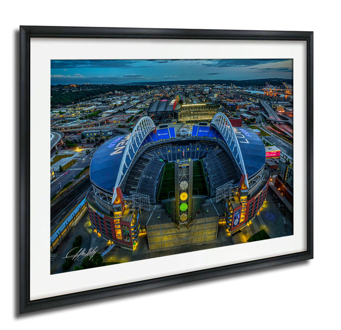 The image is a framed aerial view of a large stadium with a distinctive curved roof, surrounded by a cityscape at night.