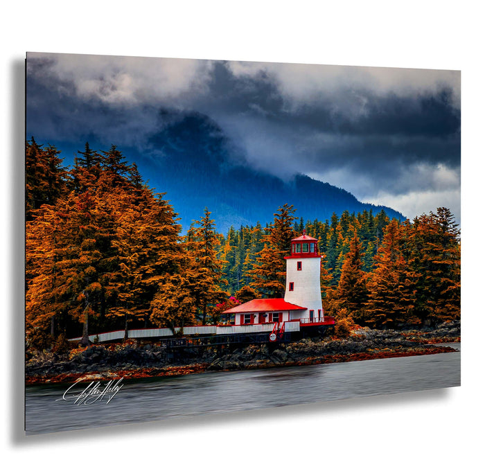A picturesque lighthouse stands on a rocky shore, surrounded by a forest of autumn-colored trees and a dramatic cloudy sky.
