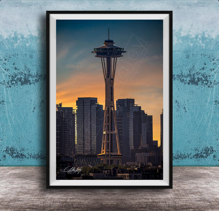 A framed photograph of the Space Needle in Seattle, with the city skyline in the background at sunset.