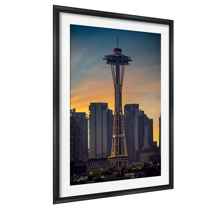 a tall, white tower with a pointed top, set against a backdrop of a city skyline at sunset.