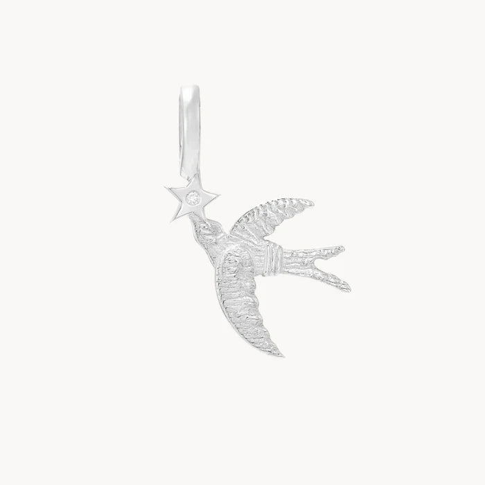 Front view of a silver pendant shaped like a flying swallow holding a five-pointed star, with a small clear stone set in the center of the star, shown on a plain off-white background.