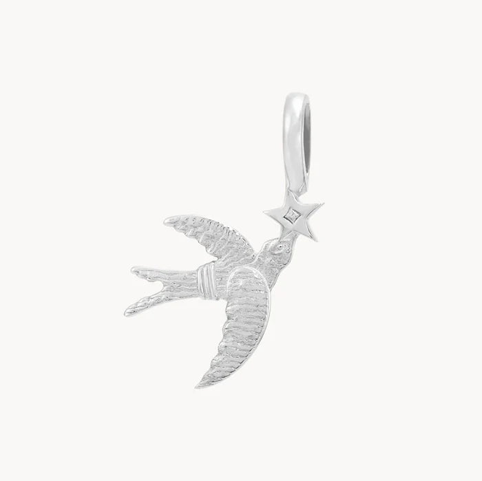 Back view of a silver pendant shaped like a flying swallow holding a five-pointed star, with a small clear stone set in the center of the star, shown on a plain off-white background.
