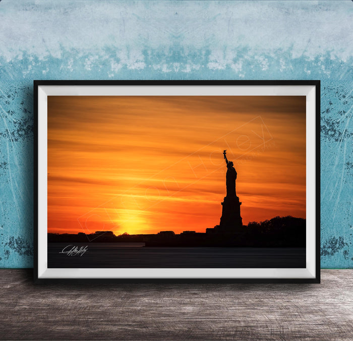A framed photograph of the Statue of Liberty silhouetted against a vibrant sunset sky.