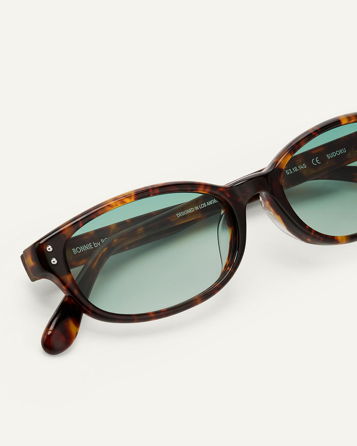Close-up shot of Bonnie Clyde Sudoku sunglasses in tortoise with green lenses.