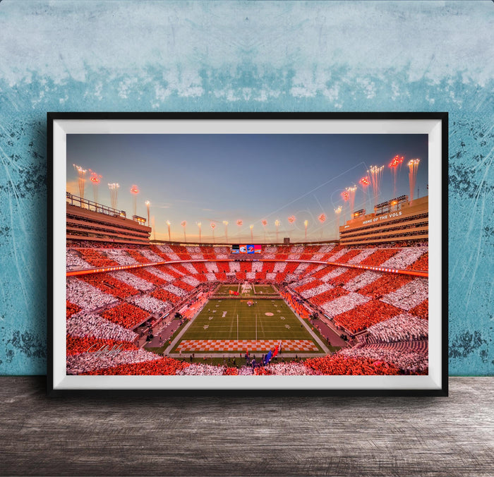A framed photograph of a football stadium at night, with the field illuminated by red and white lights and the stands filled with spectators.