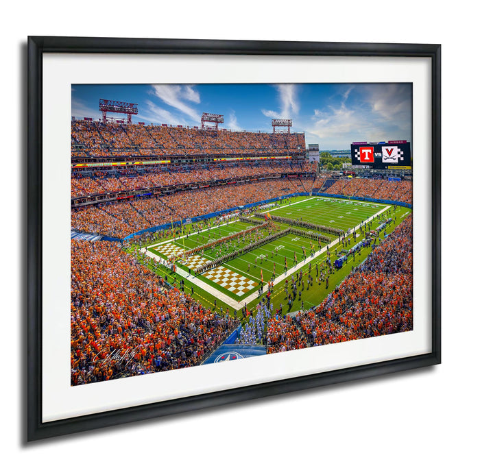 A framed image depicting a crowded football stadium with a large field, a scoreboard, and a large crowd of spectators.