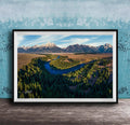 The image is a framed aerial view of a mountainous landscape with a winding river, surrounded by lush forests.