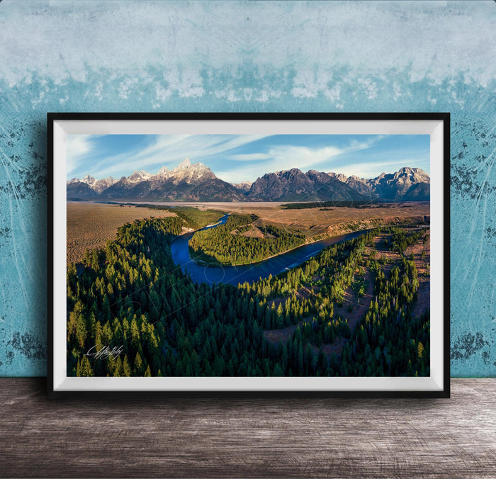 The image is a framed aerial view of a mountainous landscape with a winding river, surrounded by lush forests.