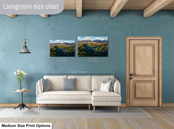 a living room with a white sofa, a wooden door, and a painting of a landscape on the wall. The painting is of a river and mountains, and it is described as a medium-sized print.