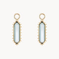 A pair of gold elongated hexagon earring charms with a london blue topaz stone surrounded by spiked edges, shown on a plain off-white background.