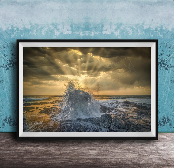 The image is a framed photograph of a dramatic ocean scene, with crashing waves and a dramatic sky filled with clouds and sunbeams.