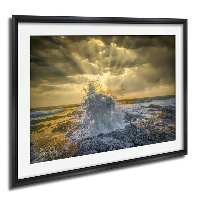 a dramatic scene of a powerful wave crashing against the rocky shore, with the sun's rays shining through the clouds and creating a stunning, golden glow over the ocean.