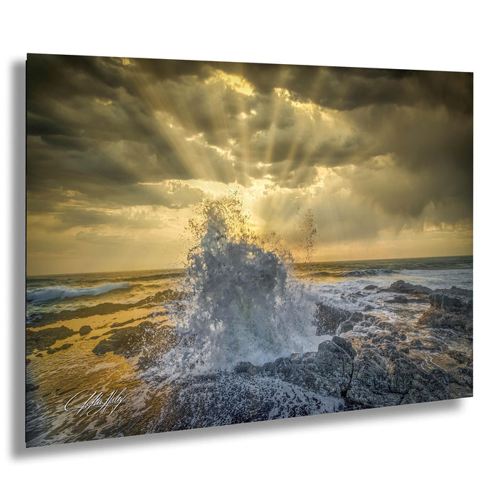 a dramatic scene of a powerful wave crashing against a rocky shore, with the sun's rays shining through the clouds and creating a stunning, golden glow over the ocean.