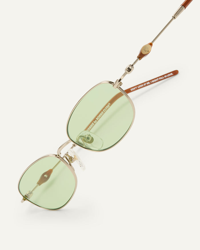 Close-up shot of Bonnie Clyde Tiptoe sunglasses in gold with green lenses.
