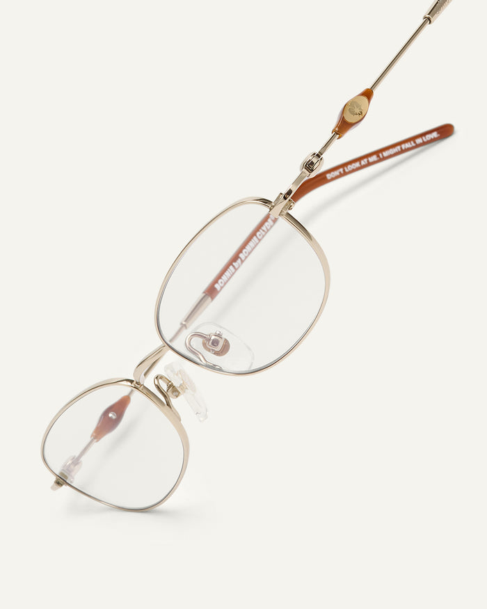 Close-up shot of Bonnie Clyde Tiptoe optical frames in gold with clear lenses.