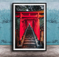 A framed photograph depicting a long, narrow red torii gate leading down a set of stairs, surrounded by lush greenery.