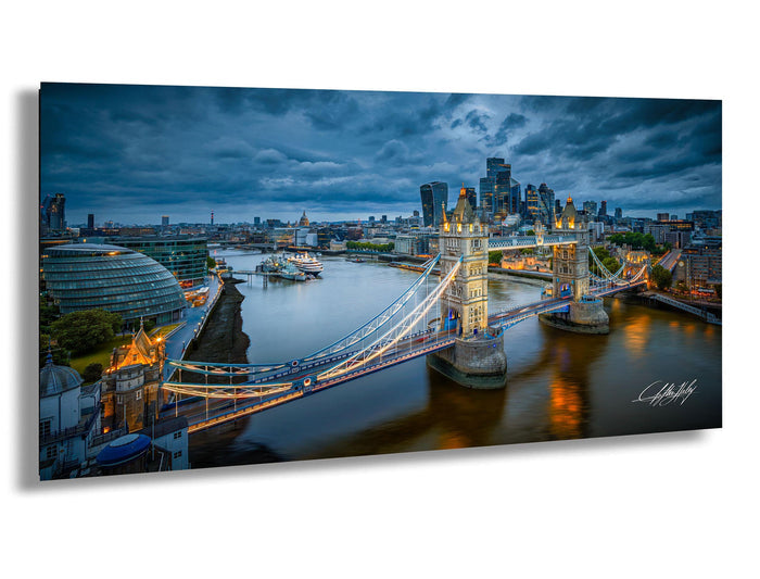 a cityscape with a large suspension bridge spanning a river, surrounded by tall buildings and a cloudy sky.