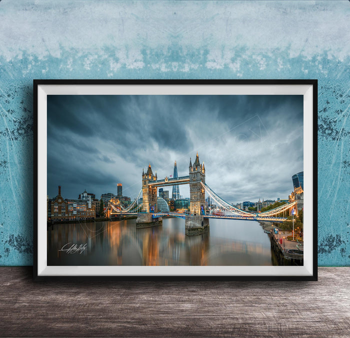 A framed photograph of the iconic Tower Bridge in London, England, with the bridge illuminated against a cloudy sky.