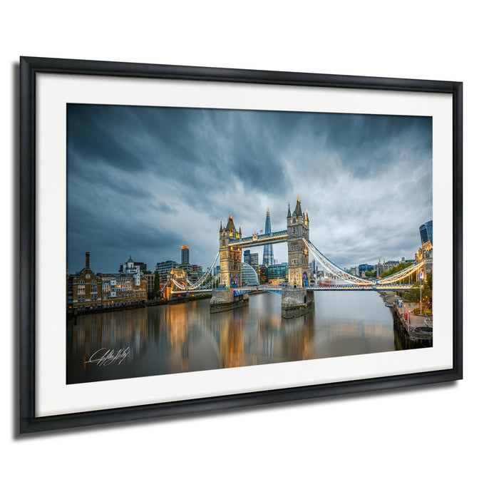 A framed photograph of the Tower Bridge in London, England, with the bridge illuminated against a cloudy sky.