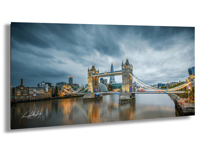 a cityscape with a large suspension bridge spanning a river, with the bridge's towers illuminated against a cloudy sky.