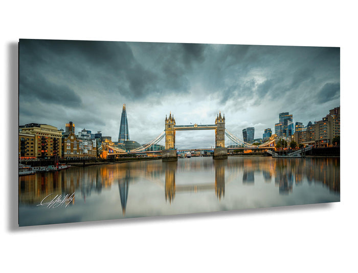 a cityscape with a large suspension bridge spanning a river, reflecting the city's skyline and the cloudy sky above.