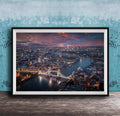 The image is a framed aerial view of a city at night, showcasing a bridge and the city skyline with illuminated buildings and a river.