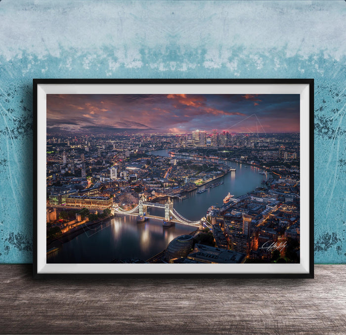 The image is a framed aerial view of a city at night, showcasing a bridge and the city skyline with illuminated buildings and a river.