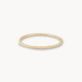A thin, gold twisted rope-style ring is displayed against a white background. The bluboho twisted stacking ring - 10k yellow gold features a delicate, minimalist design with a textured surface resembling a twisted rope.