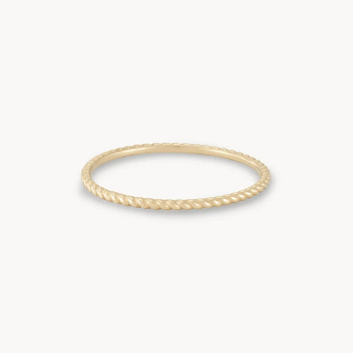 A thin, gold twisted rope-style ring is displayed against a white background. The bluboho twisted stacking ring - 10k yellow gold features a delicate, minimalist design with a textured surface resembling a twisted rope.