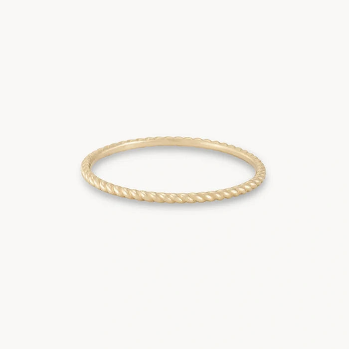 A thin, elegant twisted stacking ring - 10k yellow gold by bluboho with a twisted rope design is displayed against a plain white background. The ring is circular and delicately crafted, showcasing fine detailing that resembles a rope texture.