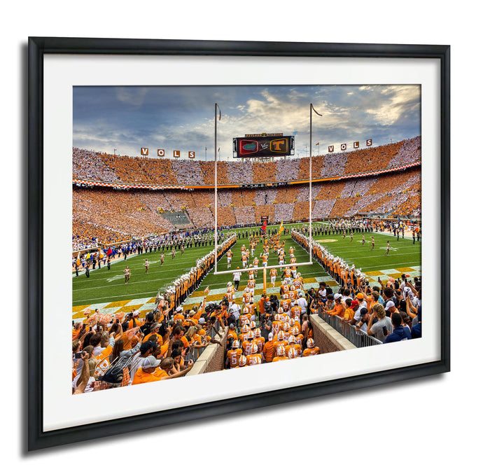 A framed photograph of a football game in progress, with a large crowd of spectators filling the stands and players on the field.
