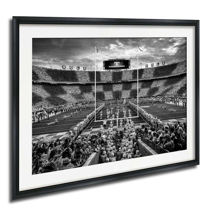 A black and white photograph of a football stadium with a large crowd of spectators, a large scoreboard, and a marching band performing on the field.