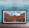 A framed photograph of a crowded football stadium with a large crowd of spectators, a large scoreboard, and a large field.