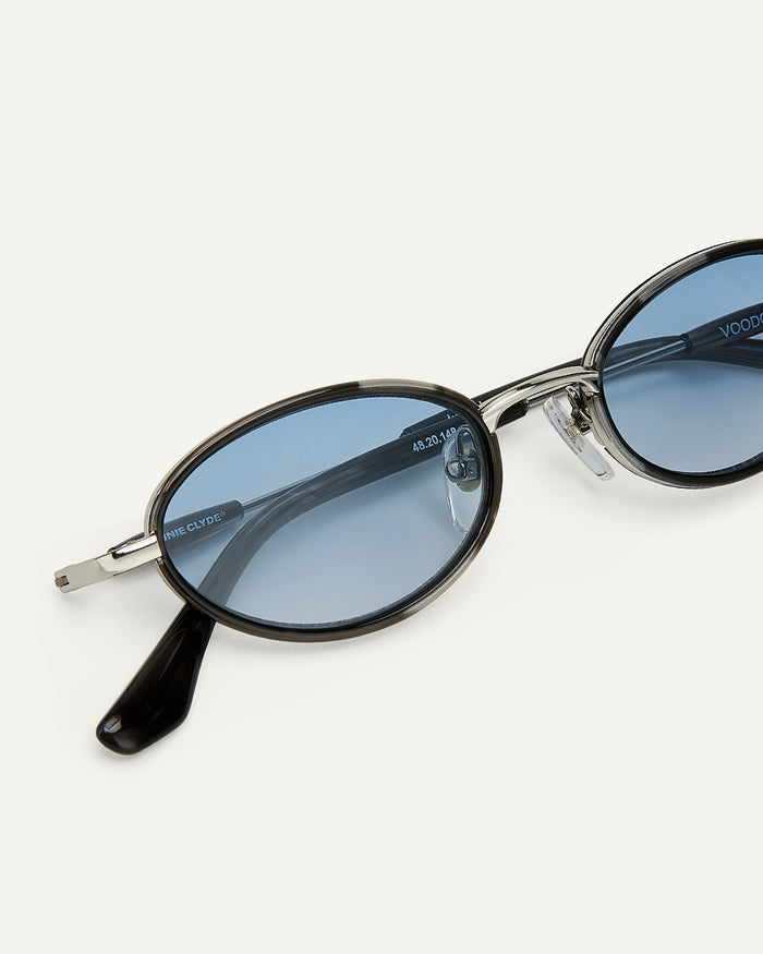 Close-up shot of Bonnie Clyde Voodoo sunglasses in silver and black tortoise with blue gradient lenses.